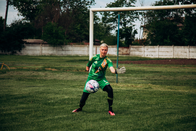 A goalkeeper in green making a save on a grass pitch