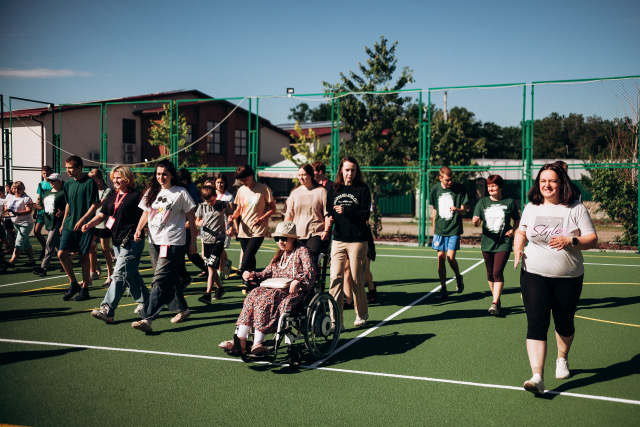 Campers and staff walking together across a green sport court, one using a wheelchair